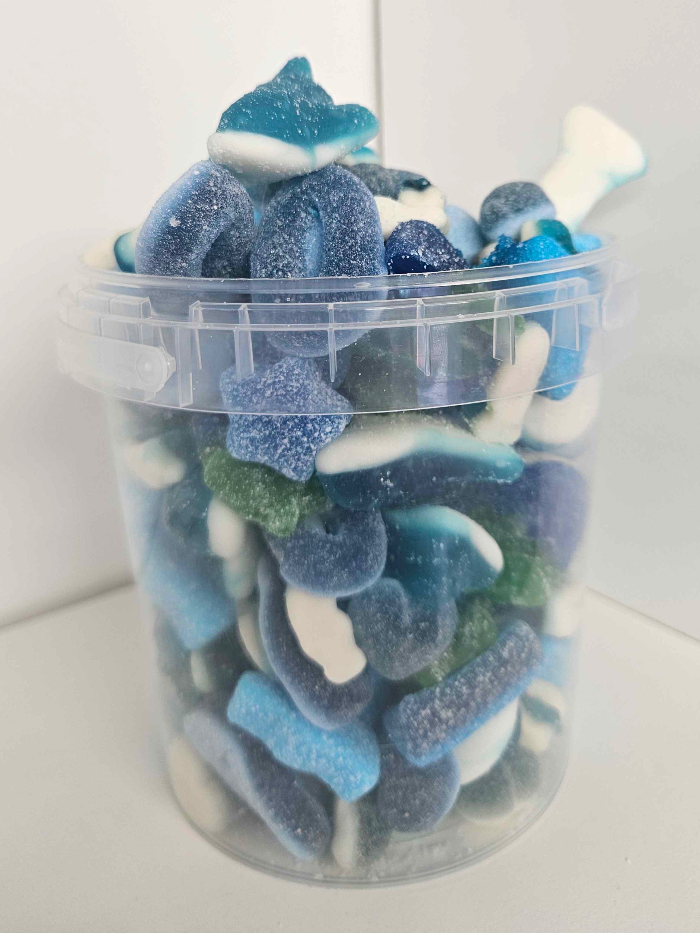 Clear container filled with blue and white gummy shark candies on a white background